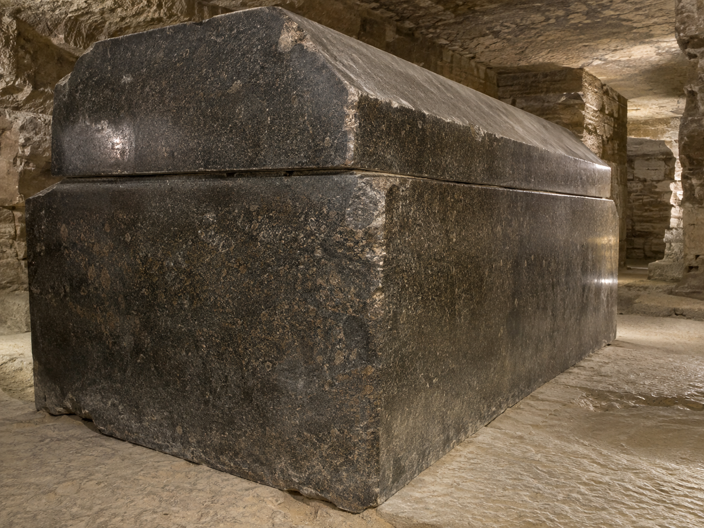 AI-generated illustrative reconstruction showing the scale of the Greater Vault, a long torch-lit underground chamber lined with massive granite sarcophagi.
